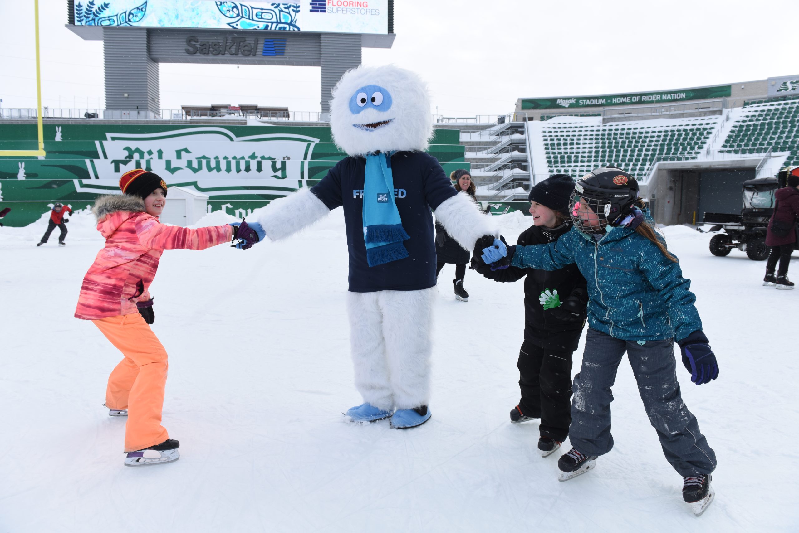 Winter mascot ice skating with children at stadium.