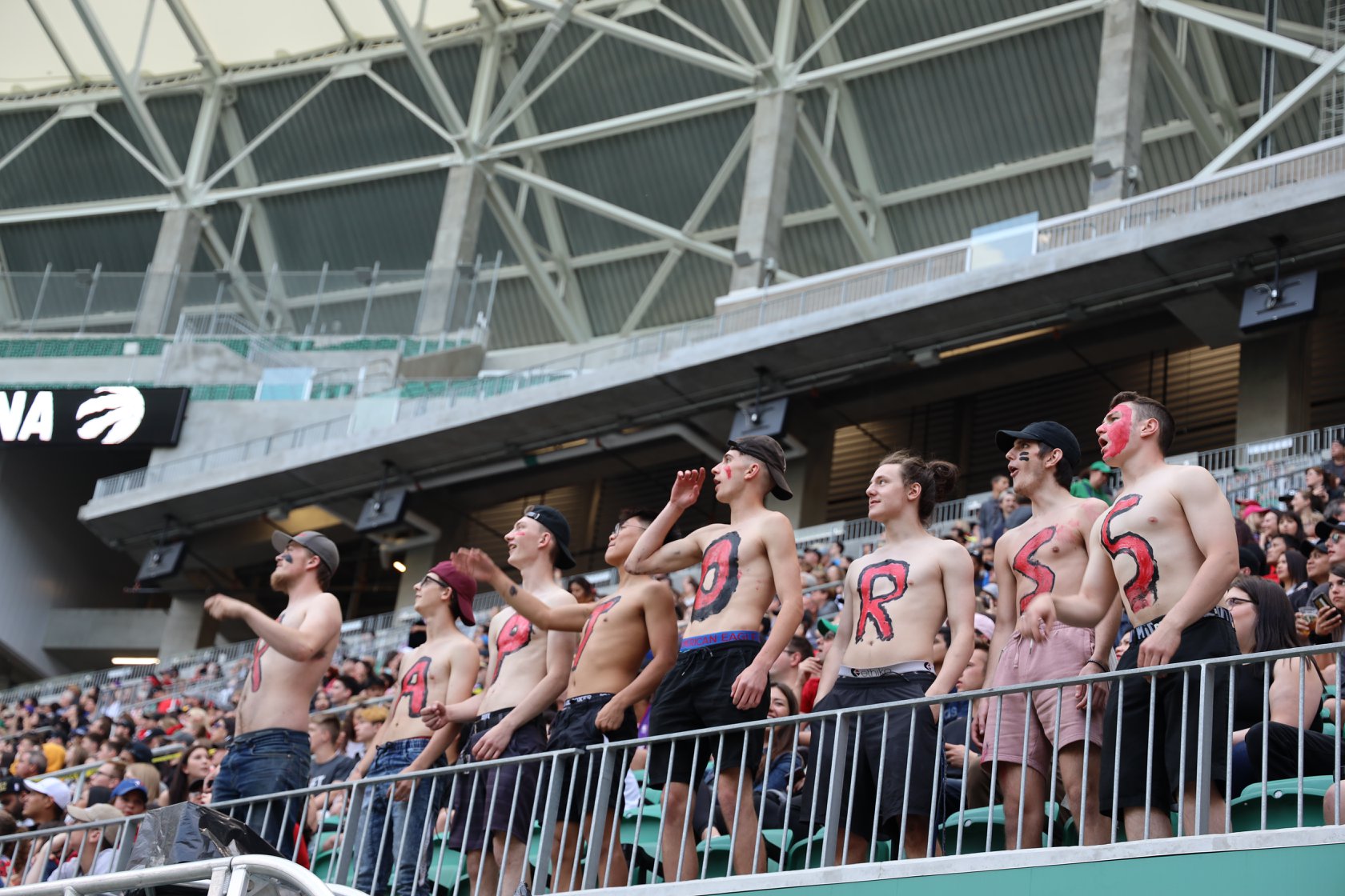 Fans with painted letters cheering at stadium.